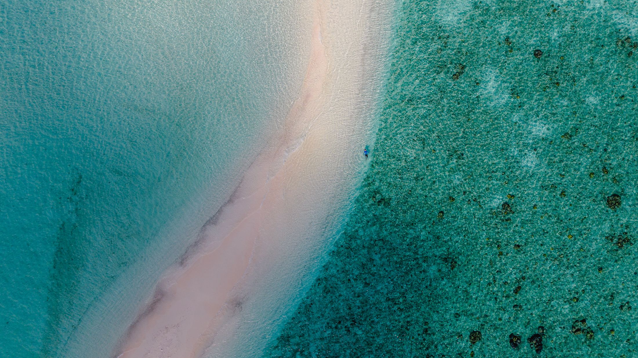 A long white sandbar between pale and deep turquoise water
