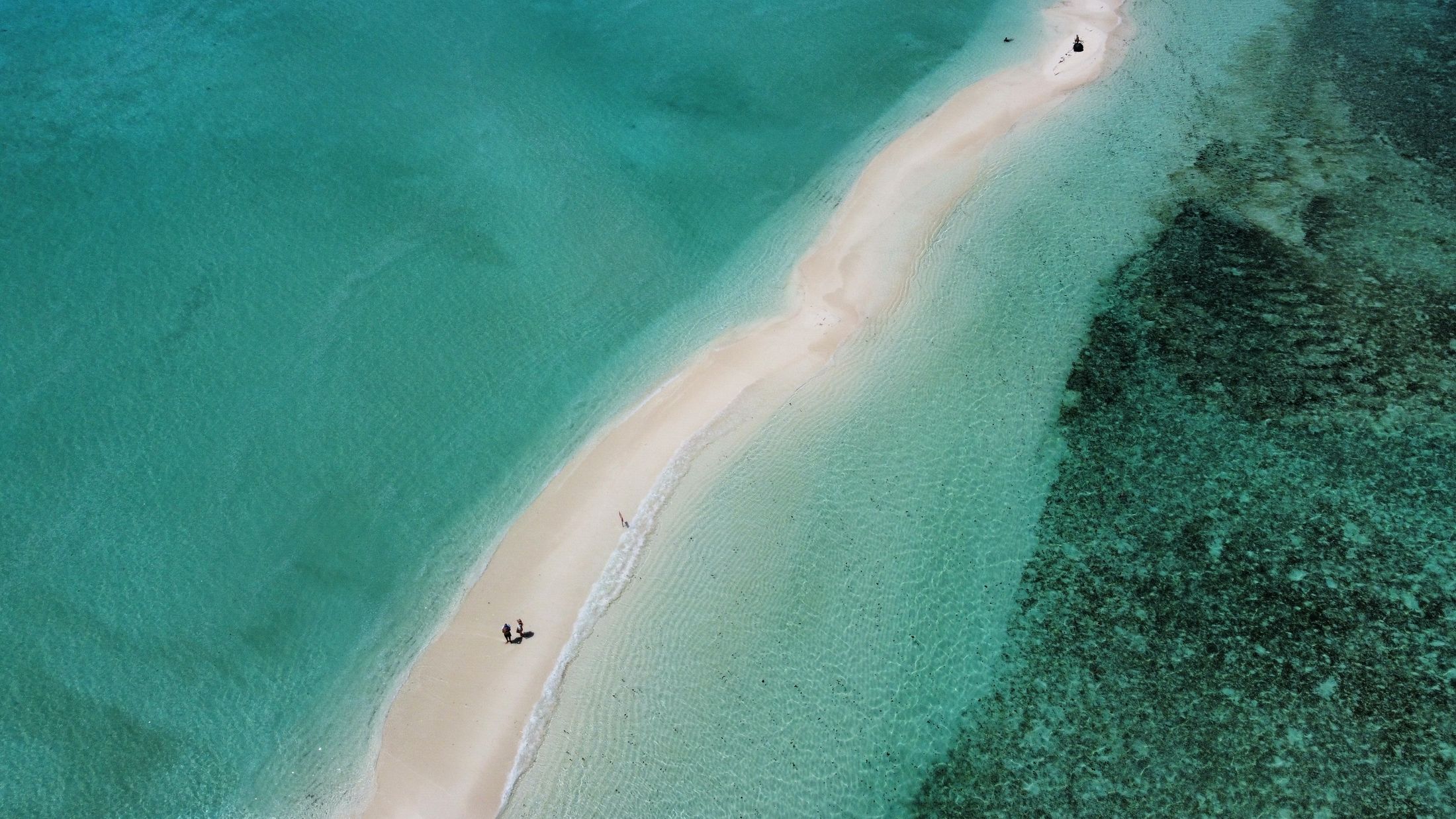 A thin white sandbar in turquoise water, from above